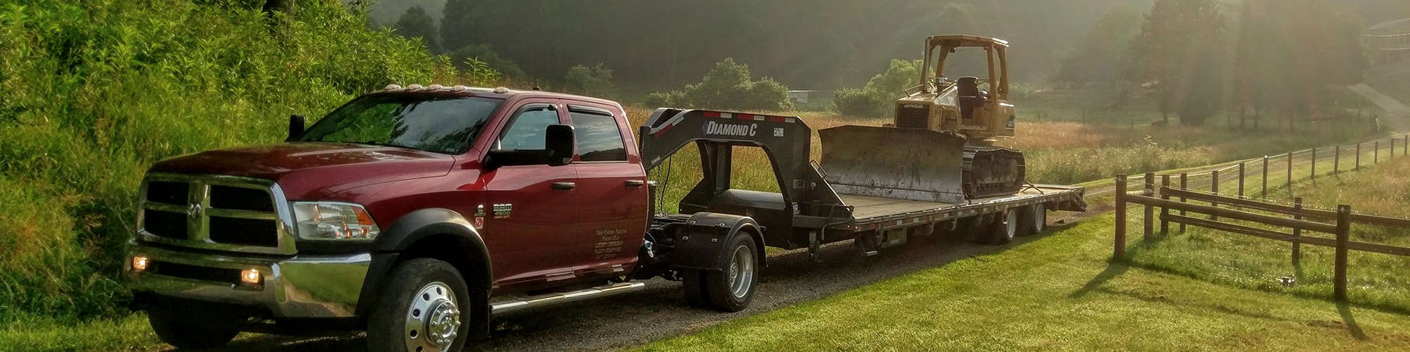 A fully loaded Diamond C trailer being pulled behind a truck with a forest landscape behind